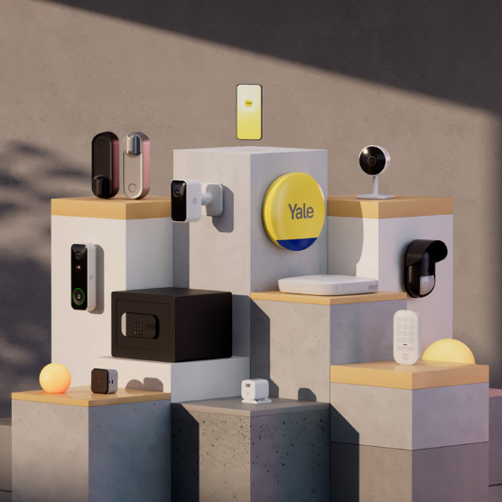 A display of smart home security devices on tiered pedestals, featuring cameras, smart locks, and a yellow Yale-branded button. 
